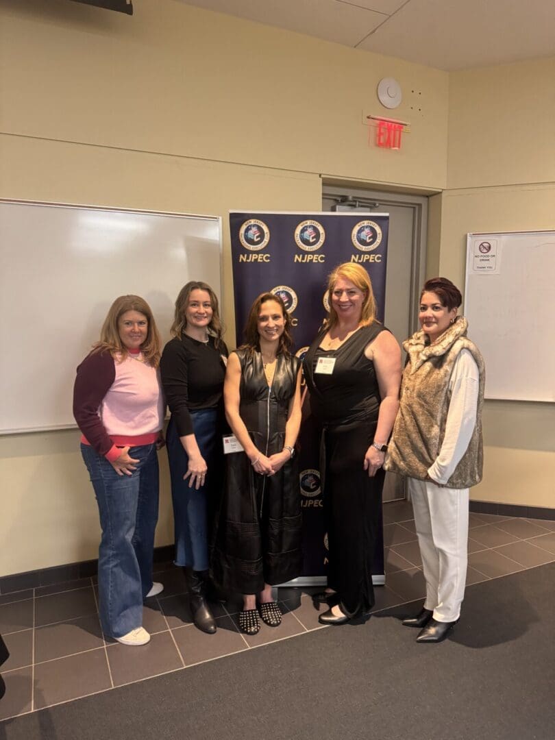 Five women stand smiling in front of an NJPEC backdrop