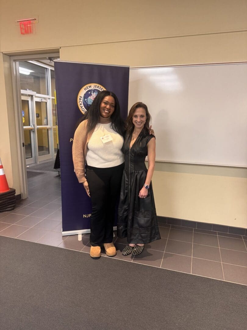 Two women smiling in front of banner.